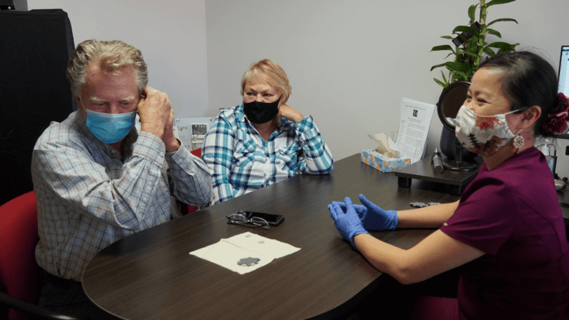 Male patient sat with wife and hearing aid specialist fitting his own hearing aid